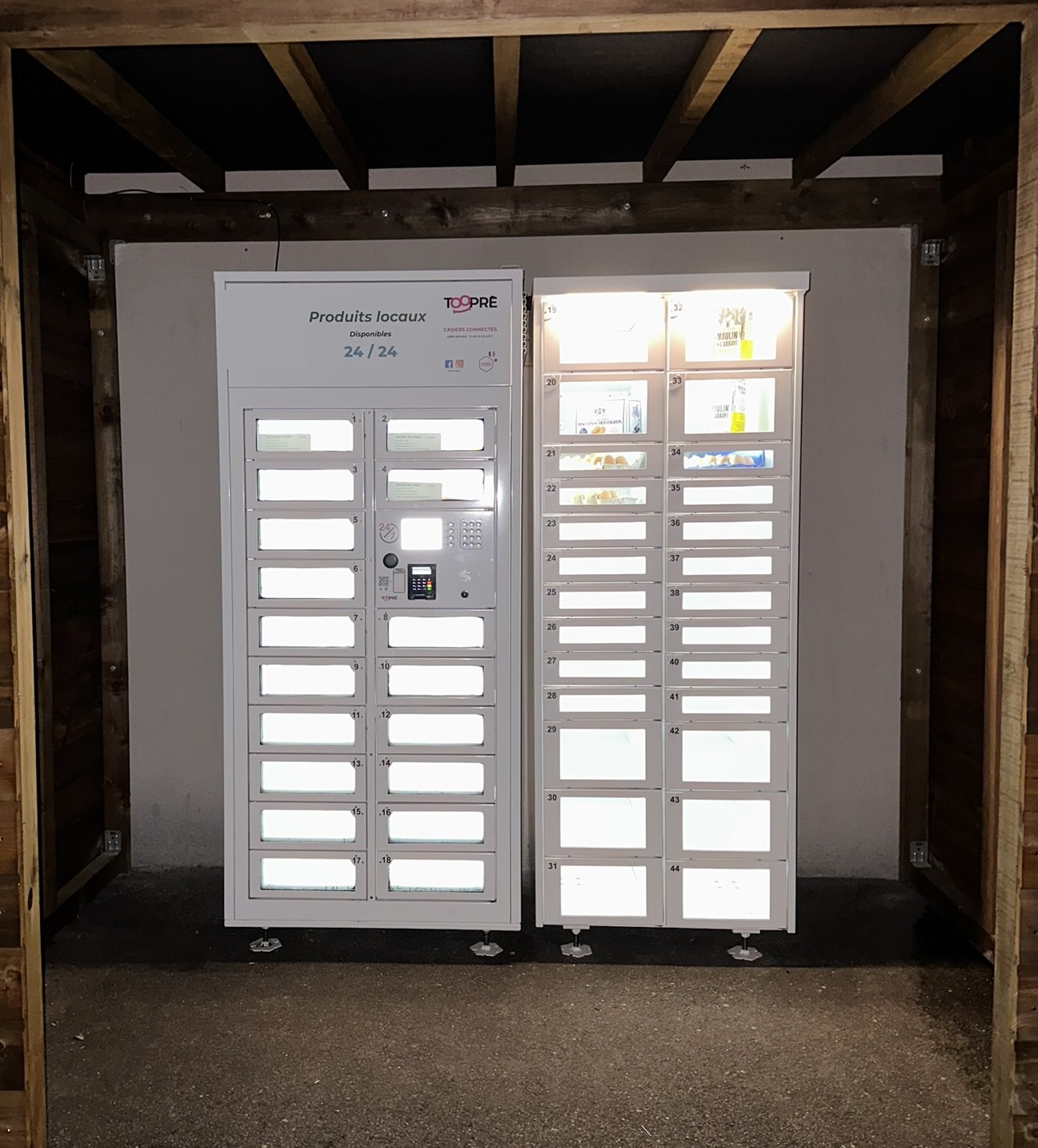 Distributeur Tooprè de produits locaux installé par une commune sous un abri en bois, éclairé de nuit
